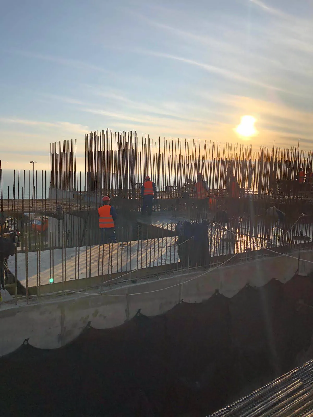 Operai al lavoro su una platea appena gettata, fra i ferri di ripresa, con il mare all'orizzonte al tramonto