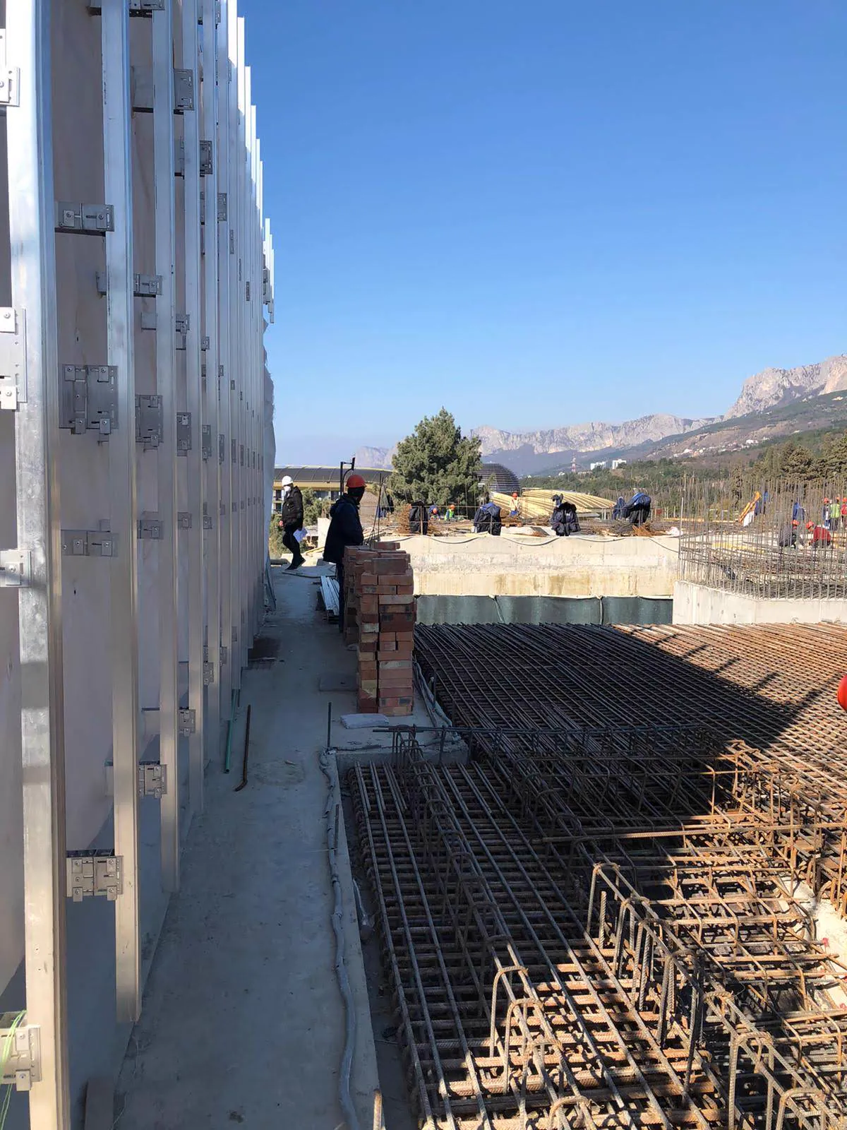 Casseri metallici e gabbie d'armatura di una fondazione, con gli operai al lavoro e le montagne sullo sfondo